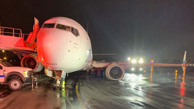 A photo of an aircraft parked on a runway at night with its landing gear broken. 