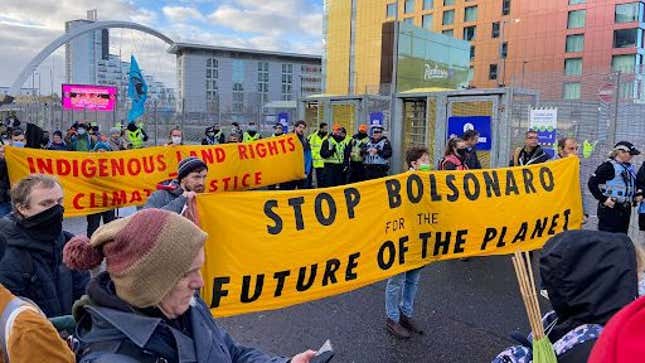 Protesters at the COP26 UN climate summit in Glasgow march down a street while carrying a banner that reads, Stop Bolsonaro for the future of the planet. Behind them, more protesters carry a banner that reads, indigenous land rights = climate justice.