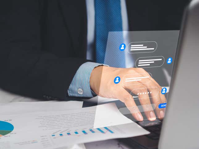 Businessman in a suit typing on a laptop keyboard with a graphic of a chat overlayed over his hand, a paper with charts is laying beside the keyboard