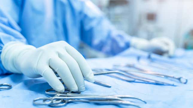 A surgeon with gloves touching their tools.