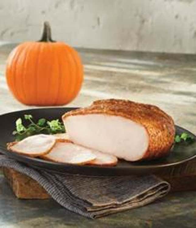 Glazed turkey sliced on a plate beside a pumpkin