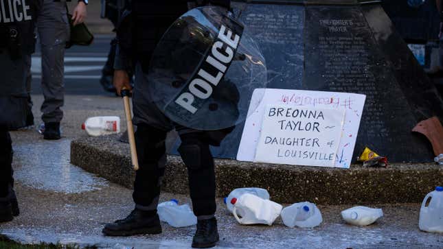 Police officers in riot gear stand in and around the milk jugs broken by two men moments earlier on May 30, 2020, in Louisville, Ky.