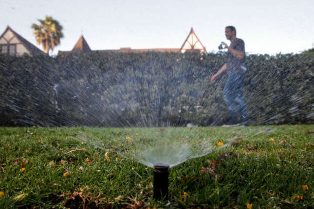 A man records sprinklers watering the lawn of a house in Beverly Hills, California, at the height of the drought in 2015.