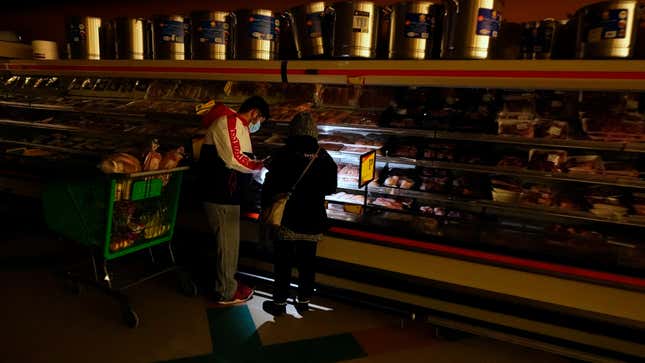 Customers use the light from a cellphone to look in the meat section of a grocery store on Feb. 16, 2021 in Dallas, Texas. Even though the store lost power, it was open for cash only sales.