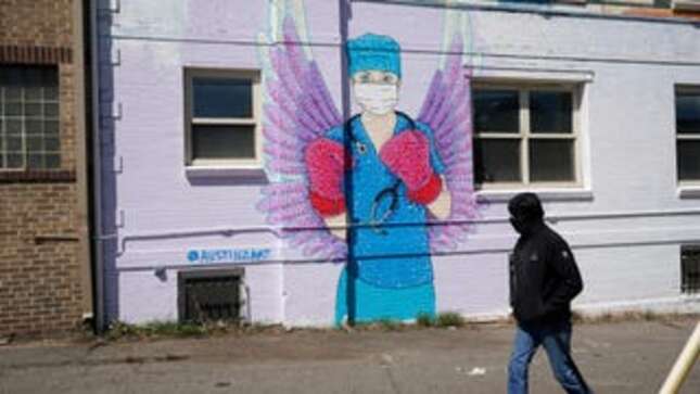 A man in a mask walks by a mural depicting a medical worker with a mask covering her mouth and nose, wearing boxing gloves and angel-like wings on her back on April 14, 2020, in downtown Denver.