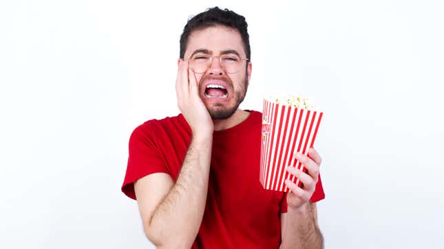 Young man in red T-shirt against white background eating popcorn, hiding face with hands pouting and crying, standing upset and depressed complaining about job problem.