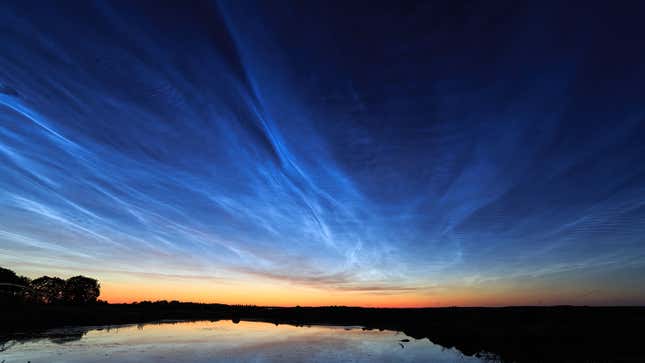 Noctilucent clouds hang over a lake at sunset.