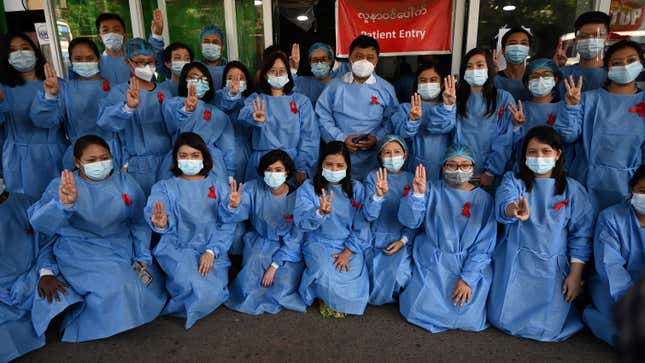Medical staff makes a three finger salute with a red ribbons on their uniform at the Yangon General Hospital in Yangon on February 3, 2021.