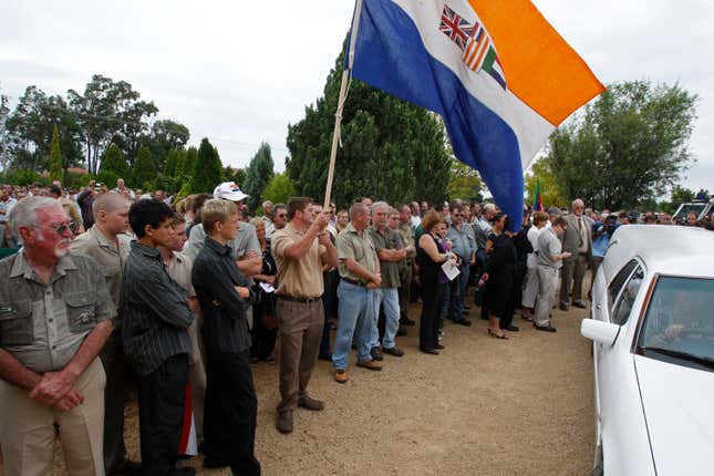 Supporters, hold a former South African apartheid government flag as slain white supremacist leader Eugene Terreblanche, coffin arrives at the church in Ventersdorp, South Africa, Friday, April 9, 2010. 