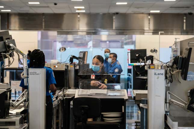 TSA agents work at a security checkpoint at the Ronald Reagan National Airport on July 22, 2020 in Arlington, Virginia. During the COVID-19 pandemic, all employees and passengers are required to wear facemasks while onboard a Delta plane