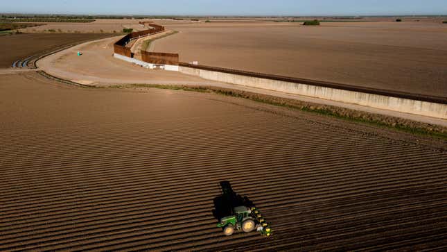 The border wall construction is seen near farmland as a tractor plows a field in Progreso, Texas