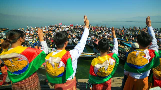 Protesters wearing traditional Shan dress make the three-figner salute as others hold signs during a demonstration against the Myanmar military coup in Inle Lake, Shan state on February 11, 2021.