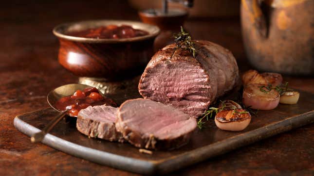 Venison rump roast on serving board beside bowl of cranberries