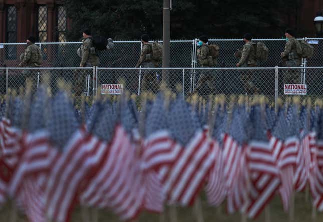 National Guard members walk past American flags placed in the ground on the National Mall as the U.S Capitol Building is prepared for the inaugural ceremonies for President-elect Joe Biden on January 18, 2021 in Washington, DC. The approximately 191,500 U.S. flags will cover part of the National Mall and will represent the American people who are unable to travel to Washington, DC for the inauguration. 