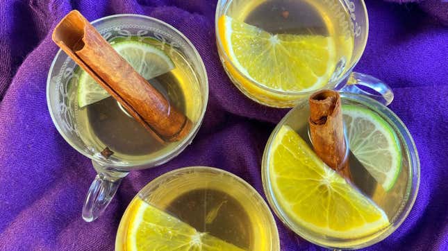 Four glasses of mulled white wine garnished with citrus and cinnamon sticks