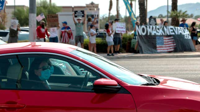 People wearing masks drive past protestors rallying against a mask mandate in Las Vegas, Nevada on August 22, 2020.