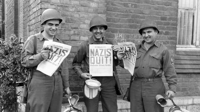 U.S. Ninth Army soldiers smiling while holding copies of ‘The Stars and Stripes’ announcing Germany’s surrender in World War II. 8th May 1945.