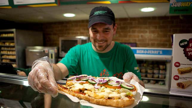 Subway employee handing off a footlong sub over the counter
