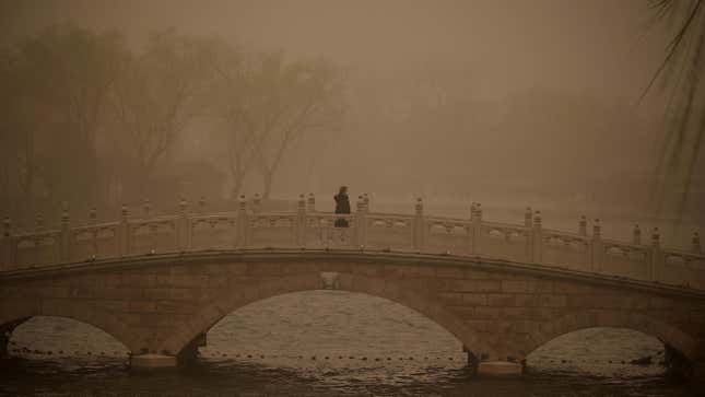 A woman crosses a bridge at Houhai lake during a sandstorm in Beijing on March 15, 2021. 
