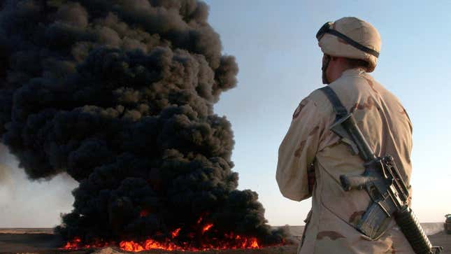 A giant black cloud of burning oil rises behind a U.S. Army soldier in August 2003.