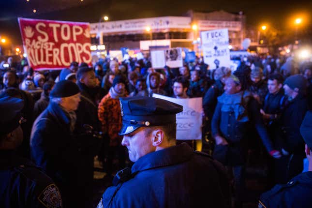 Police officers protect people entering the Barclays Center for a Brooklyn Nets game while demonstrators protest a Staten Island, New York grand jury’s decision not to indict a police officer involved in the chokehold death of Eric Garner in July on December 8, 2014 in New York City.