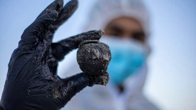 An Israeli soldier wearing a full protective suit holds a piece of tar from an oil spill in the Mediterranean Sea during a cleanup operation.
