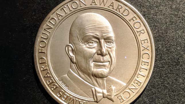 A golden James Beard Award Medallion against a black background